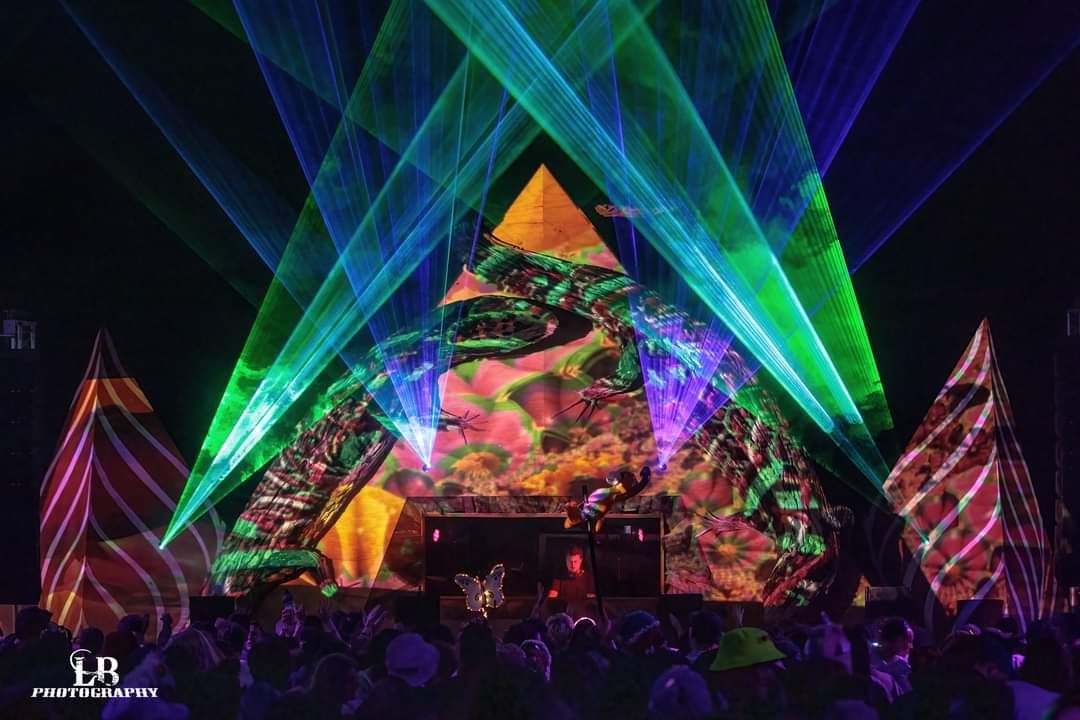 Green and blue lasers cut through swirling smoke patterns above a colourfully lit stage