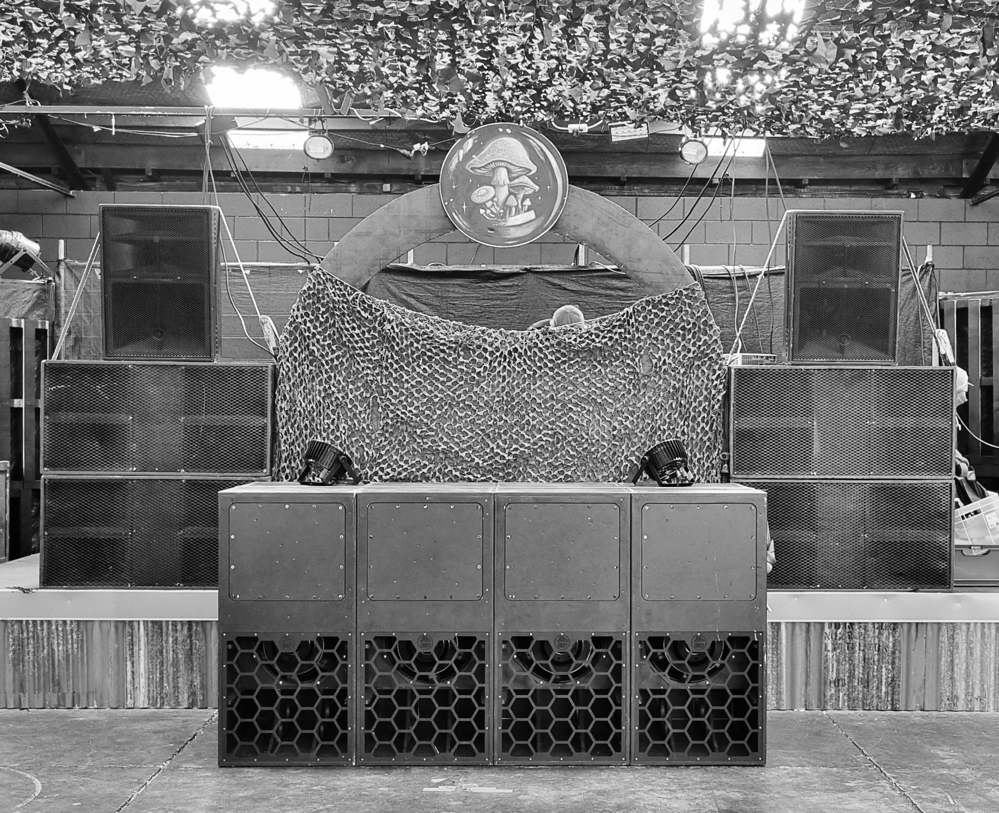 Black and white image of speaker stages around a stage, covered with camo nets