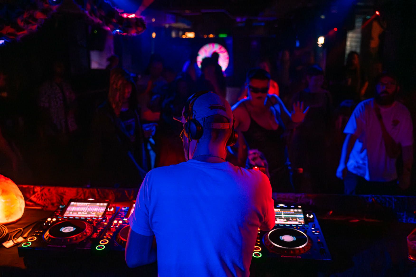 A shot from behind the DJ, lit by blue and red lights