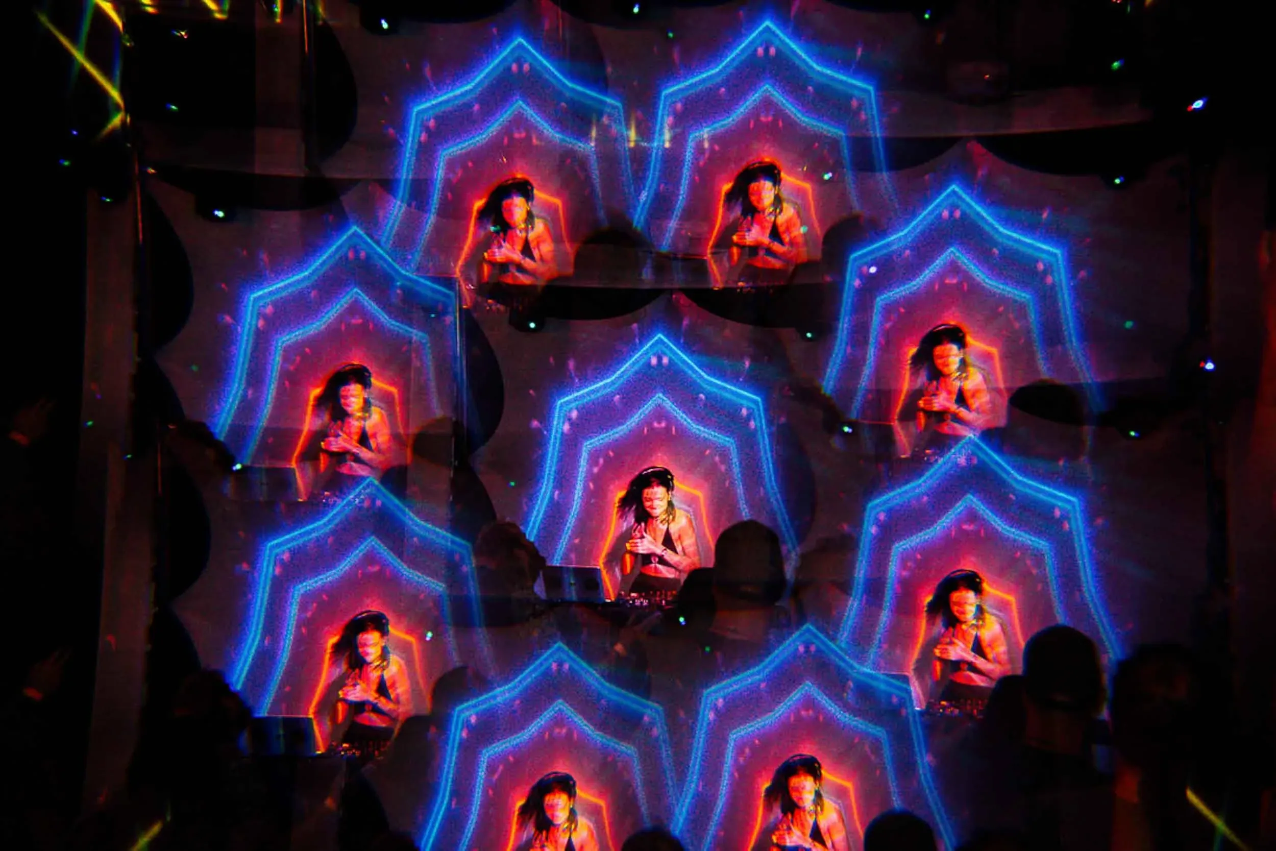 A kaleidoscope image of a femme DJ, diffracted and repeated, surrounded by colourful lights