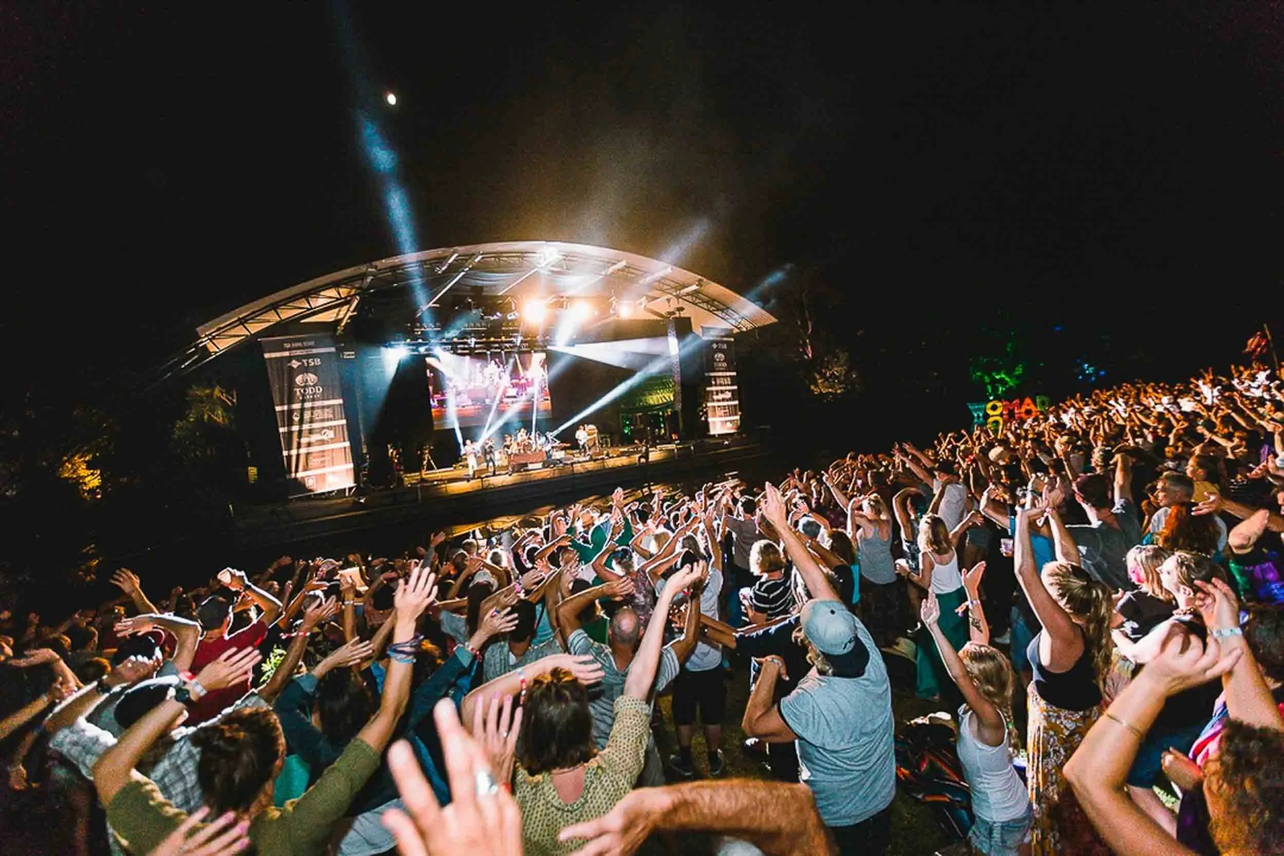 A shot over a massive crowd, hands in the air, with the stage visible in the background