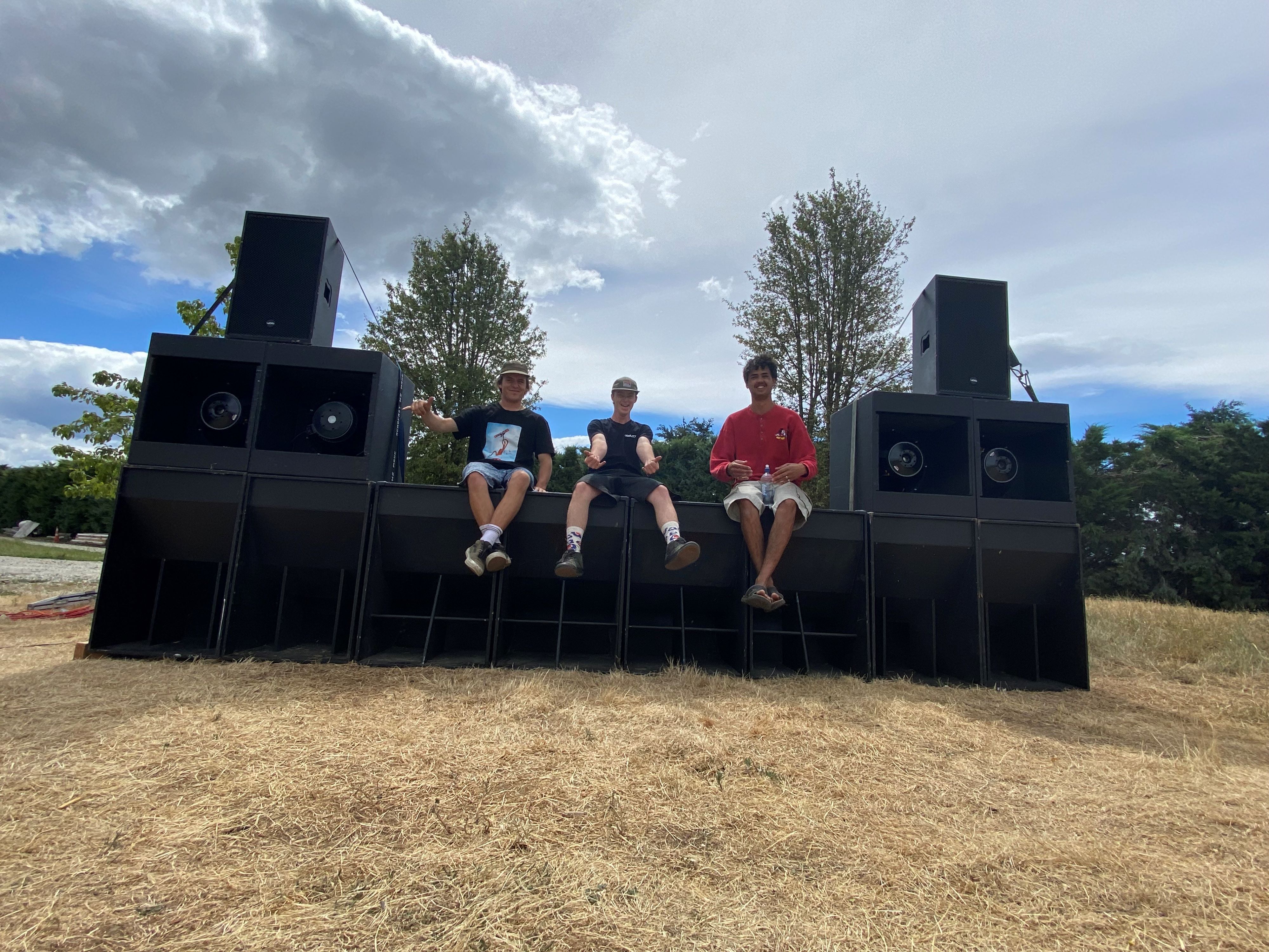The rig outdoors in a paddock, with cloudy bright skies and trees in the background. Three people are sitting on the rig looking at the camera.
