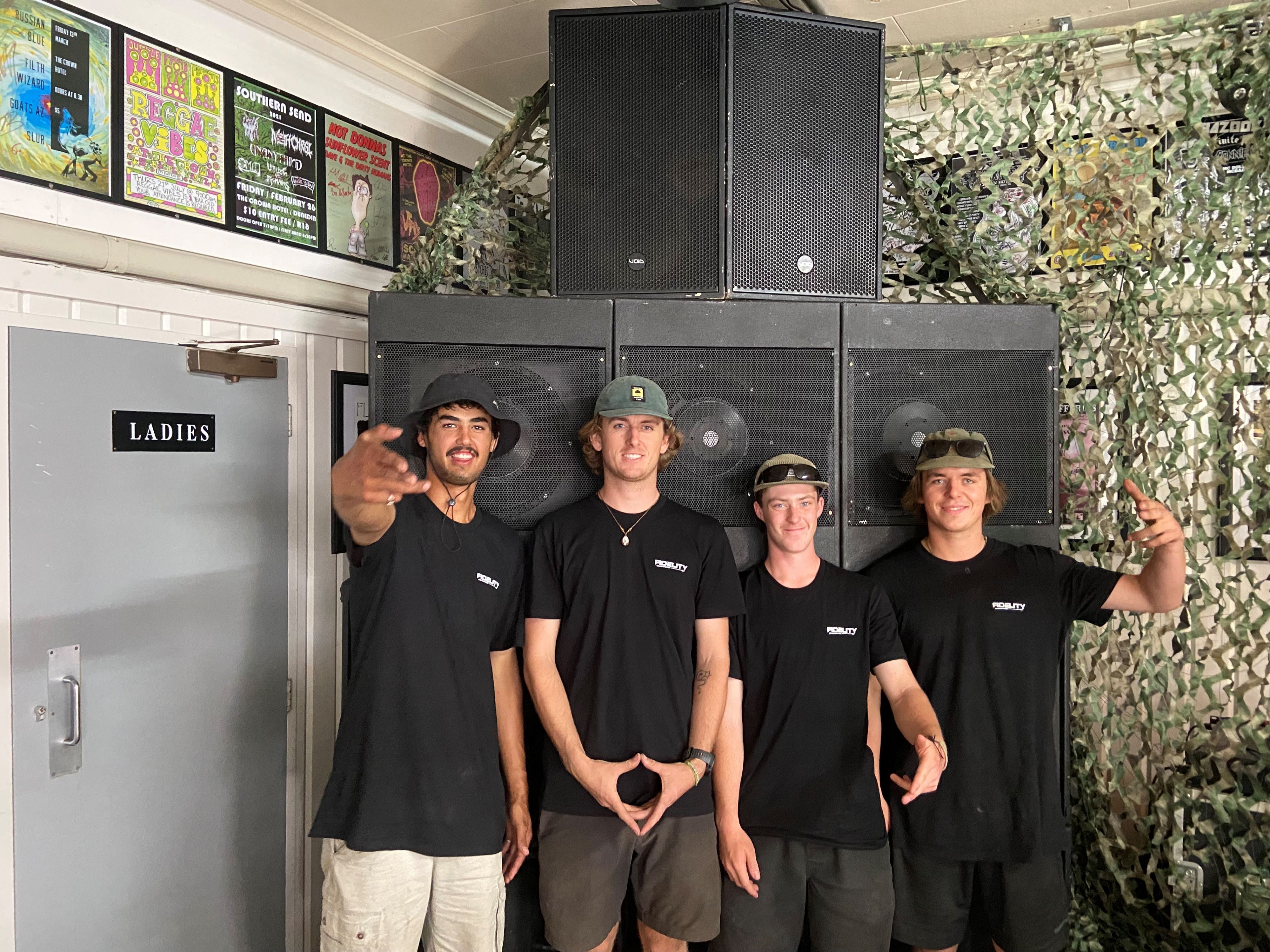 Four guys standing in front of a soundsystem, all with matching black tees