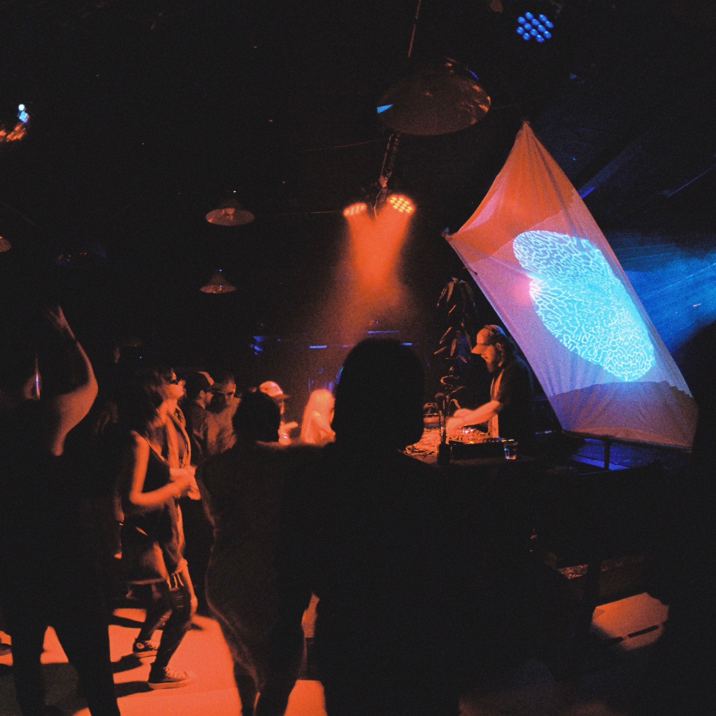 A crowd dances in front of merging shapes projected on a screen