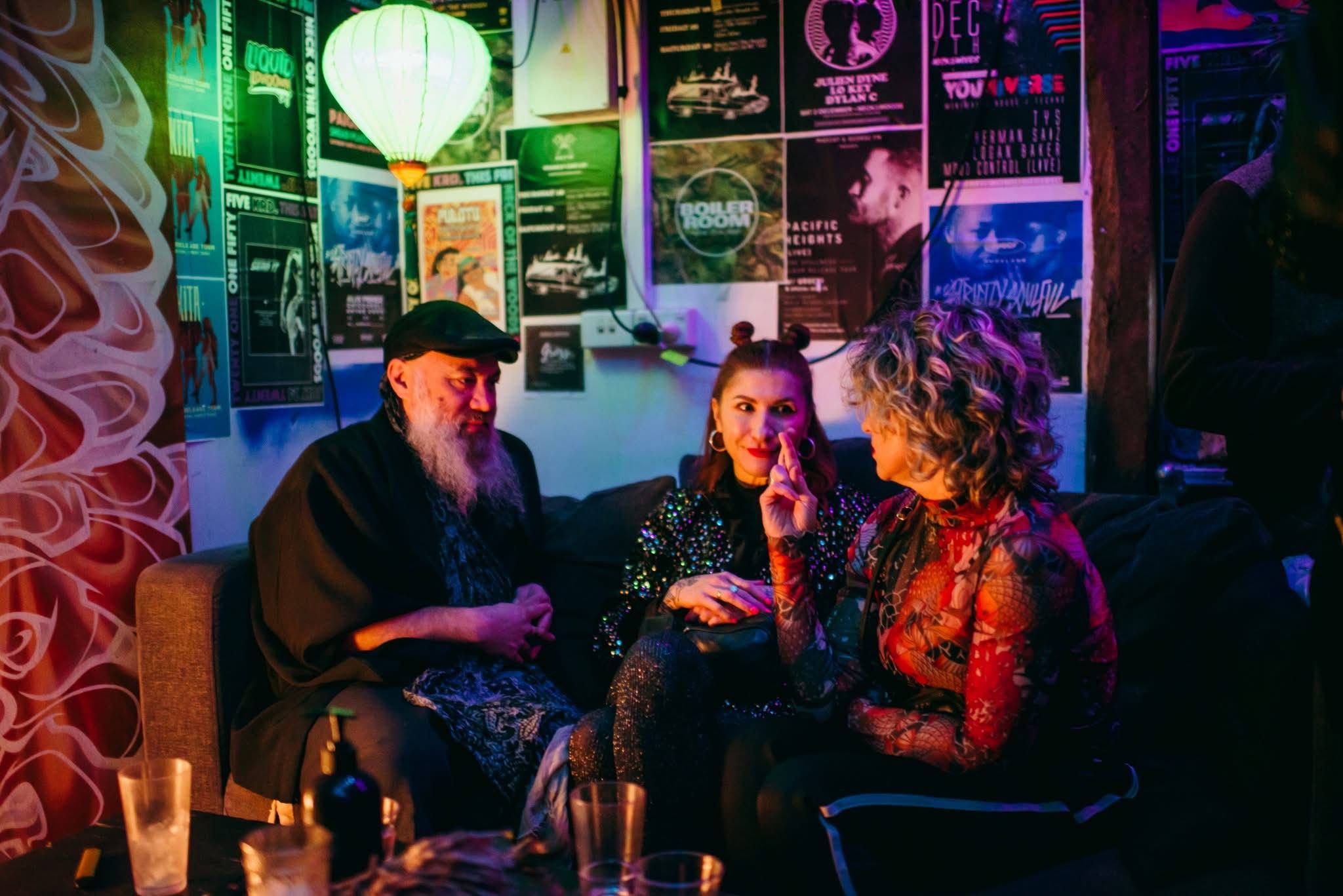 three people sitting around a table under a wall covered in posters