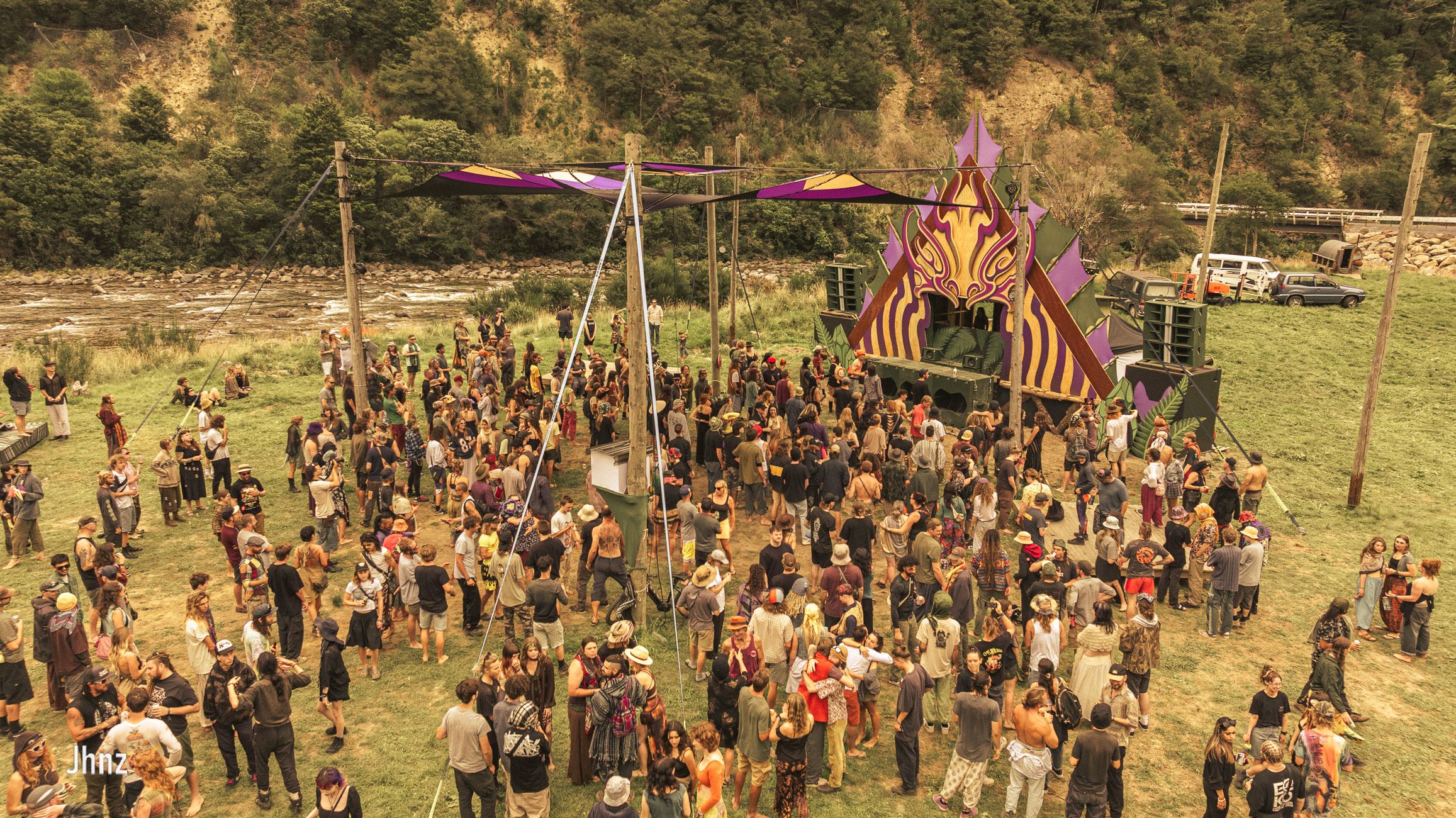 A daylit shot of a crowd in front of a decorated stage, with native bush in the background