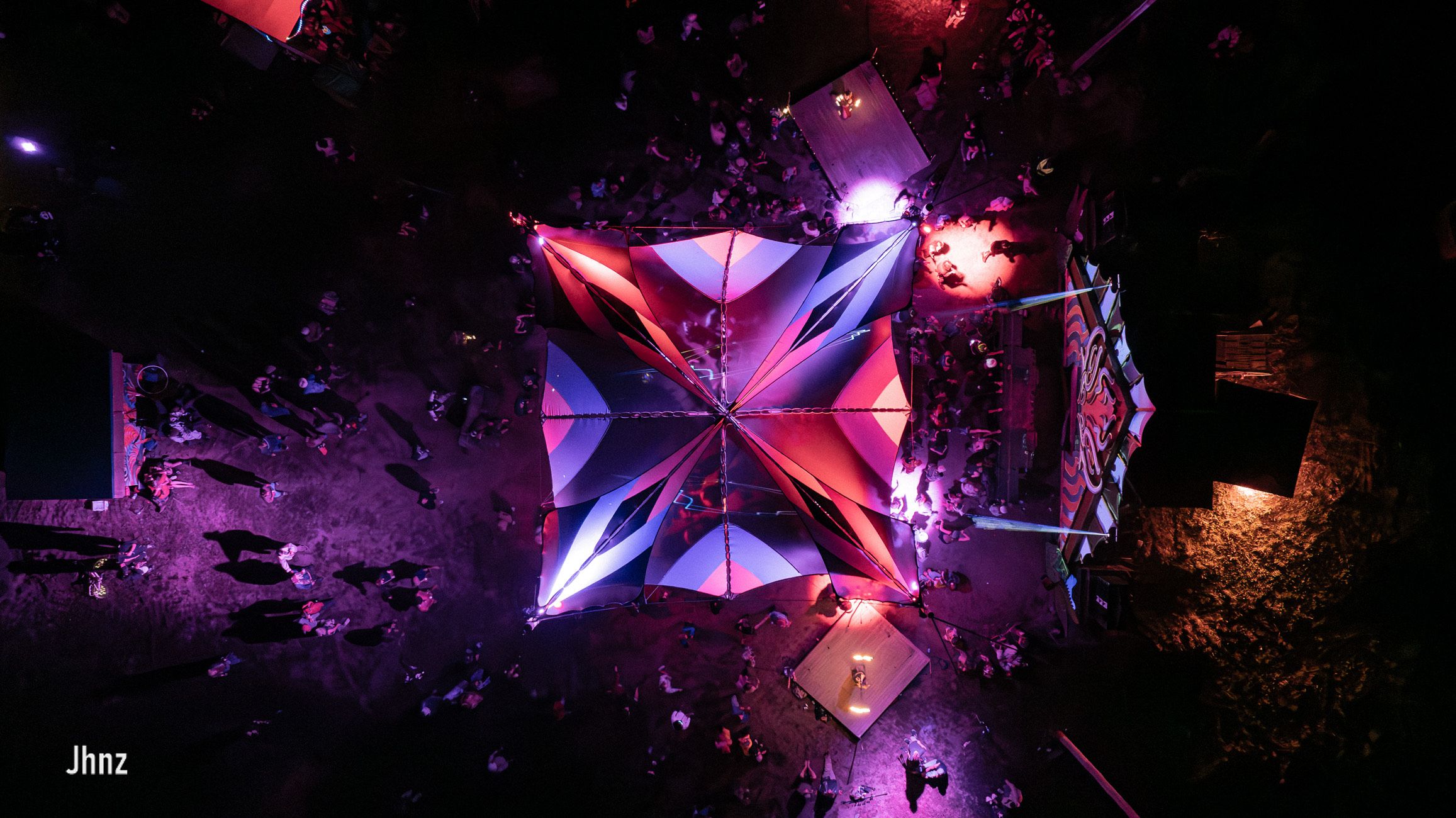 A night-time arial view of the dancefloor and stage, lit up with purples and reds glowing through the shade sails