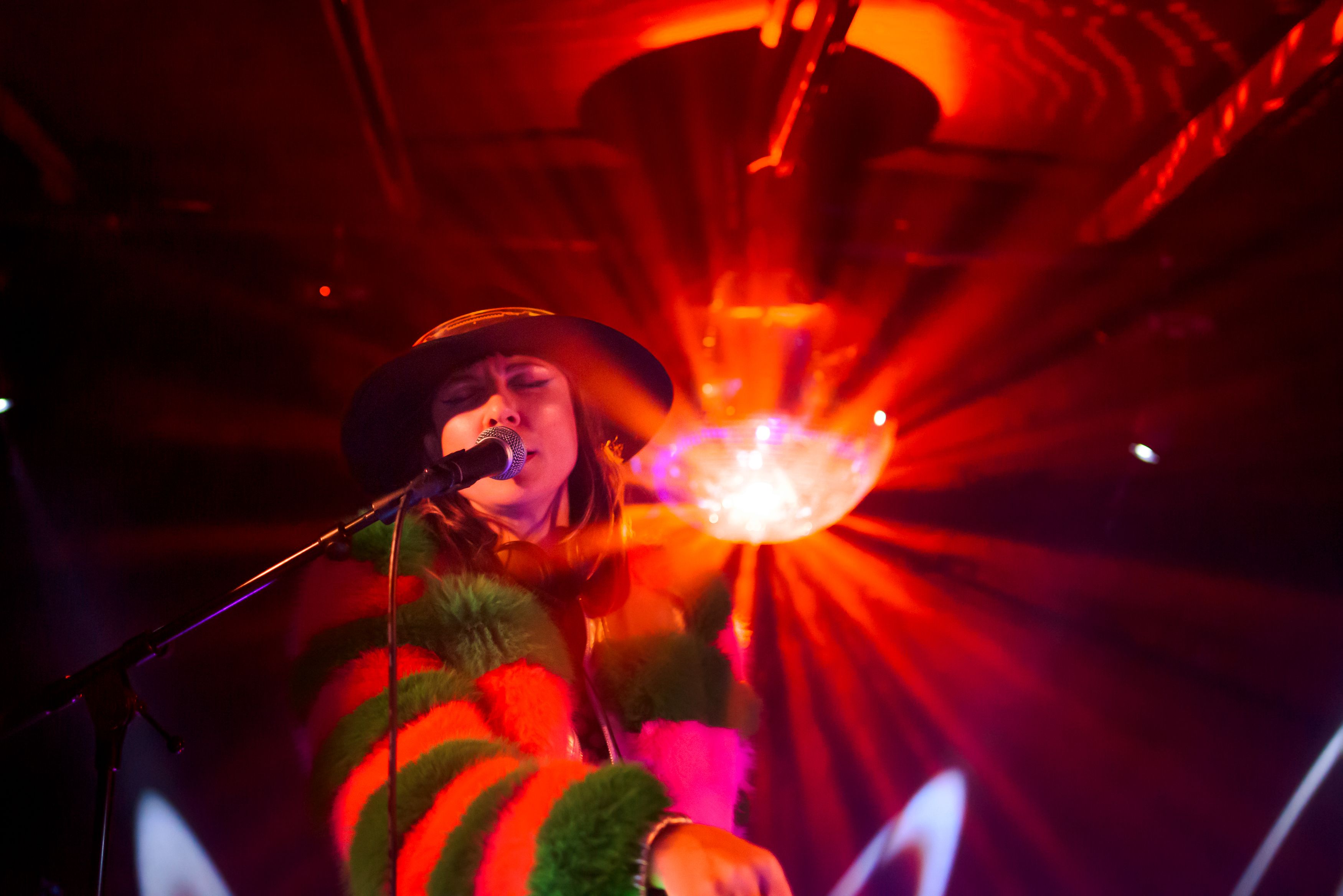 A singer caught mid note, eyes closed, with warm red light diffracting off a disco ball behind them 