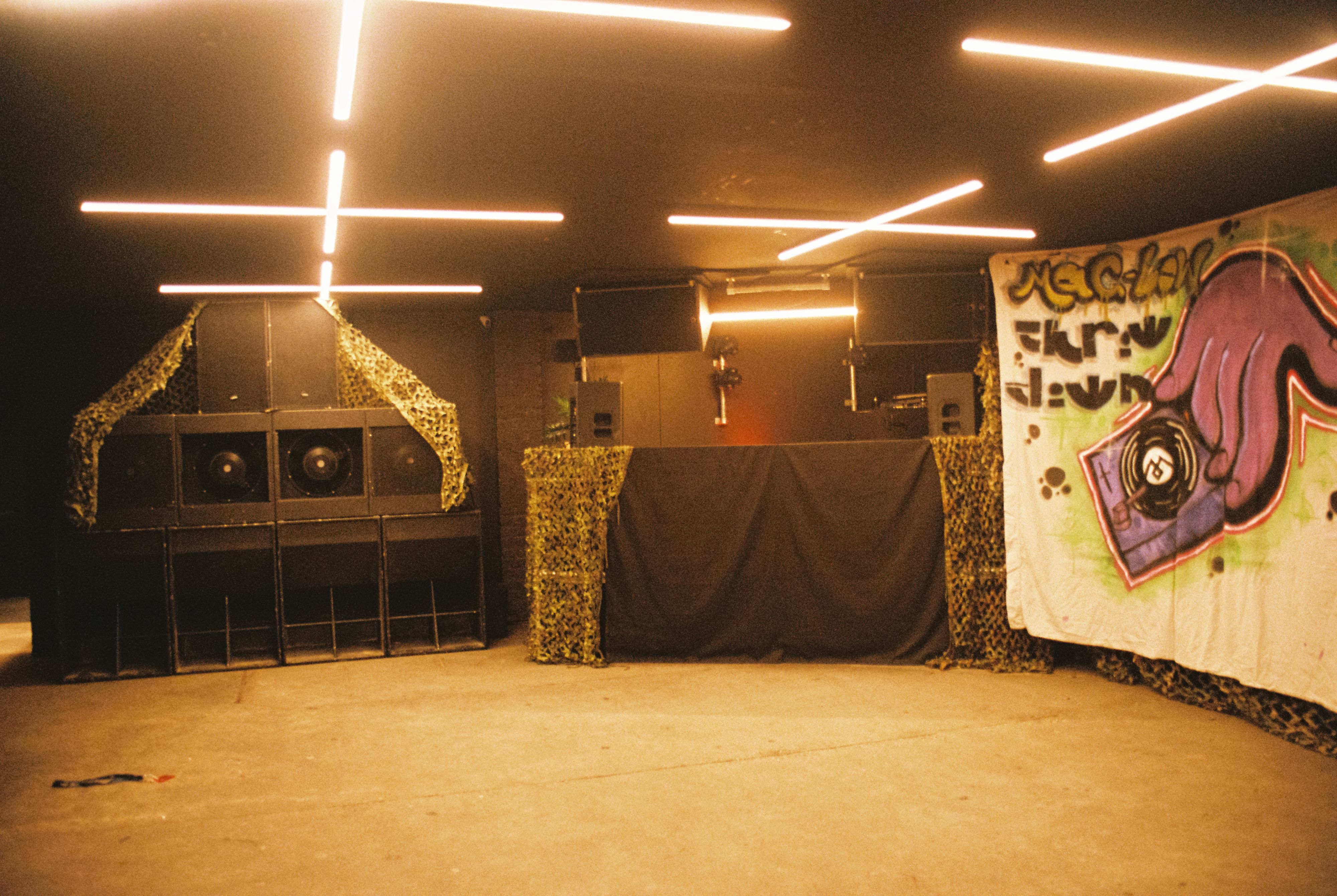 The rig set up around a DJ booth in an indoor venue, with warm bar lights crossing the ceiling