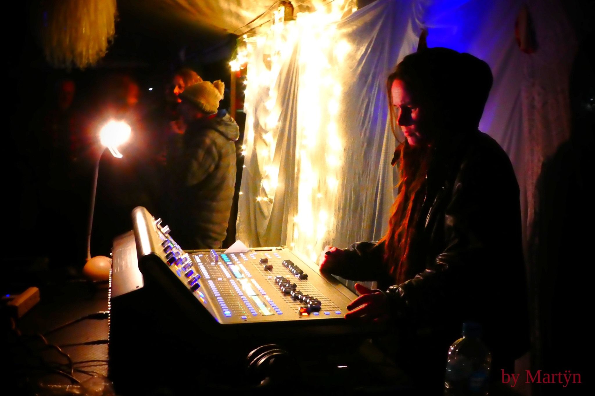 A side-on shot of Heather at the sound desk, lit up in the background by bright rope lights