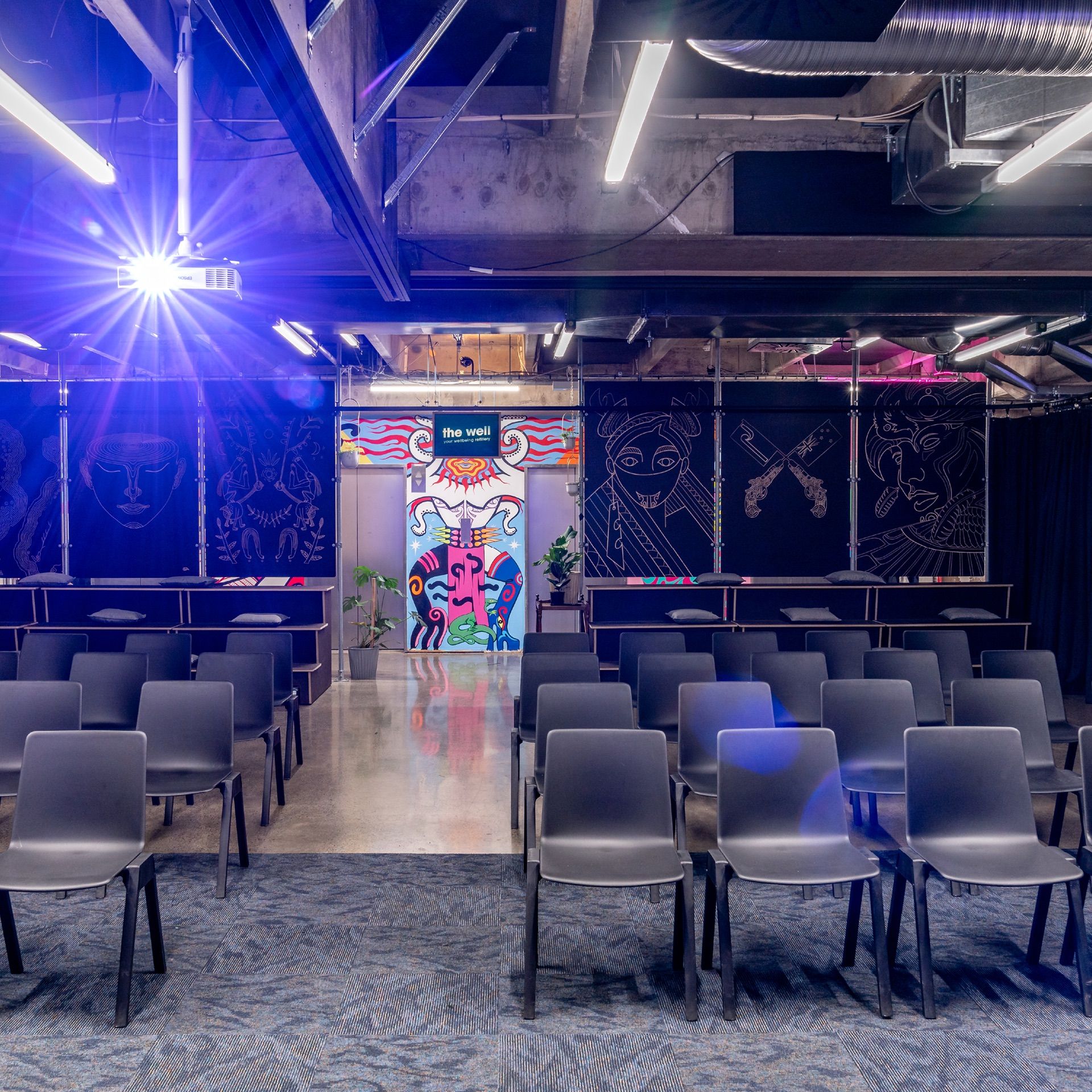 A large room with rows of chairs. At the back of the room you can see the colourful Dreamgirls mural.